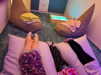 In einem gemütlich eingerichteten Raum zum Snoezelen liegen 3 Kinder auf einem Sitzsack. Zu sehen sind nur die Beine der Kinder.