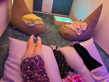 In einem gemütlich eingerichteten Raum zum Snoezelen liegen 3 Kinder auf einem Sitzsack. Zu sehen sind nur die Beine der Kinder.