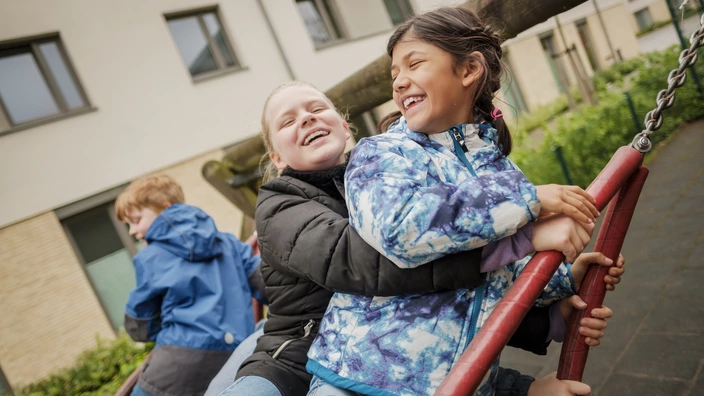  Drei Kinder schaukeln gemeinsam in einer Nestschaukel und lachen dabei